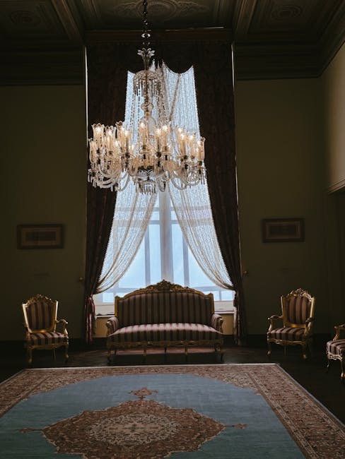 A pink upholstered sofa with ornate rolled arms and a mix of decorative cushions, including velvet and textured fabric, is positioned against a plain beige wall in a living room. The sofa's seat cushions feature a red damask pattern, and the upholstery appears clean and well-maintained. The sofa is set on a pink patterned area rug with a floral motif, and the room is illuminated by soft, natural lighting, emphasizing the plush texture and bright colors. Visible behind the sofa are a white baseboard and light wooden flooring. This image represents surface cleaning and maintenance as offered by Haringey Carpet Cleaners, highlighting deep cleaning and sanitisation for upholstery in domestic settings.
